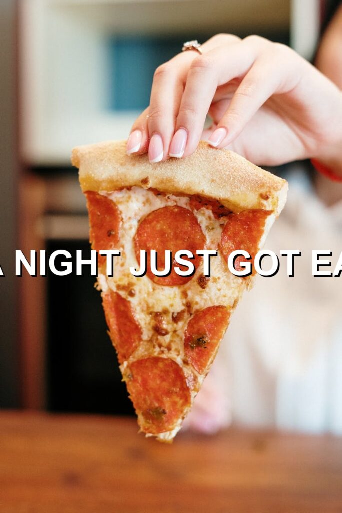 Freshly baked pizza slice with melted cheese and pepperoni, held by a person's hand against a rustic wooden backdrop.