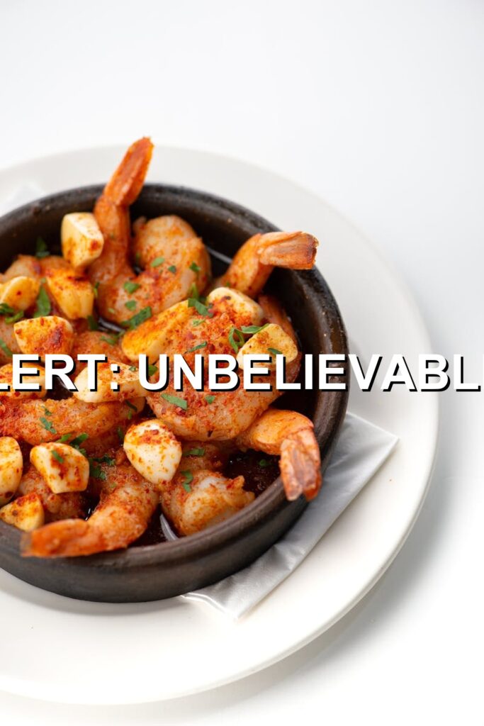 Crispy shrimp pasta bathed in a rich, savory sauce served in a black dish, ready to be enjoyed.